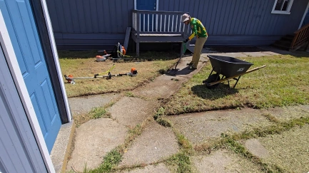 Crew member edging a stone walkway with a wheelbarrow nearby